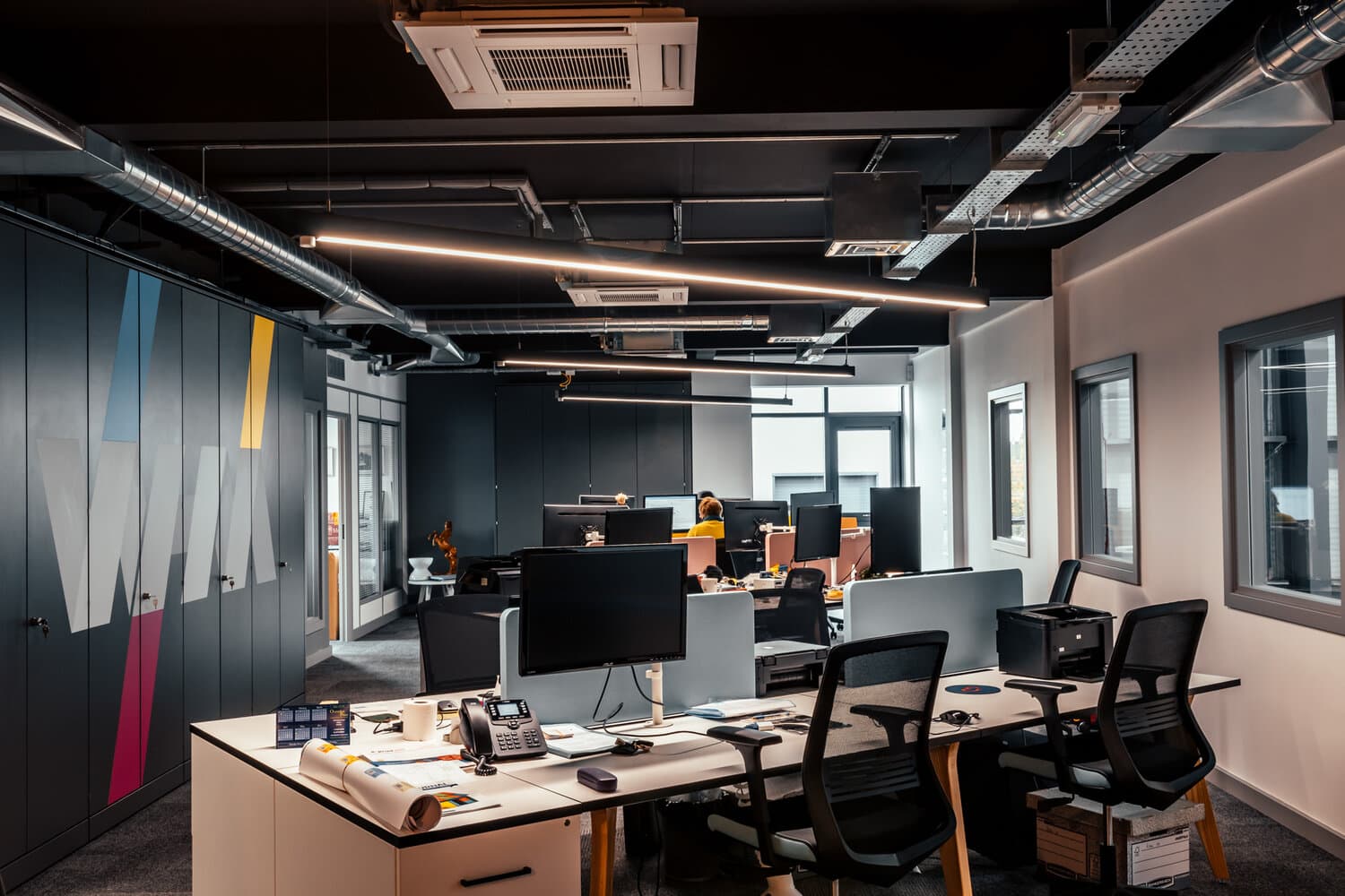 Modern open-plan office with desks, monitors and exposed network infrastructure